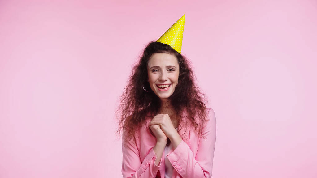 sonriente joven con gorra de fiesta durante el cumpleaños aislado en rosa  - Foto, imagen