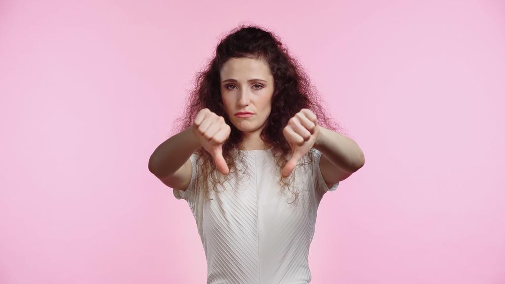 незадоволена молода жінка показує великі пальці вниз ізольовані на рожевому
 - Фото, зображення