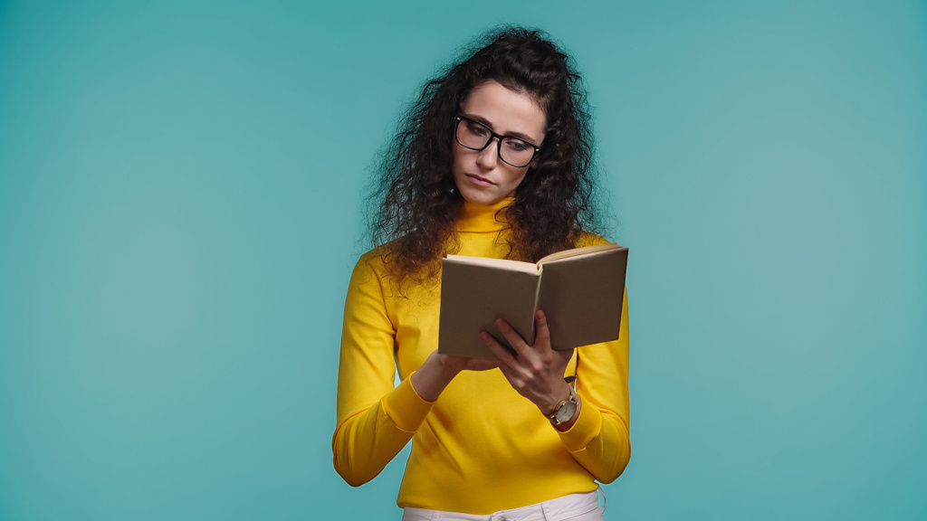 concentrated woman in glasses reading book isolated on blue - Photo, Image
