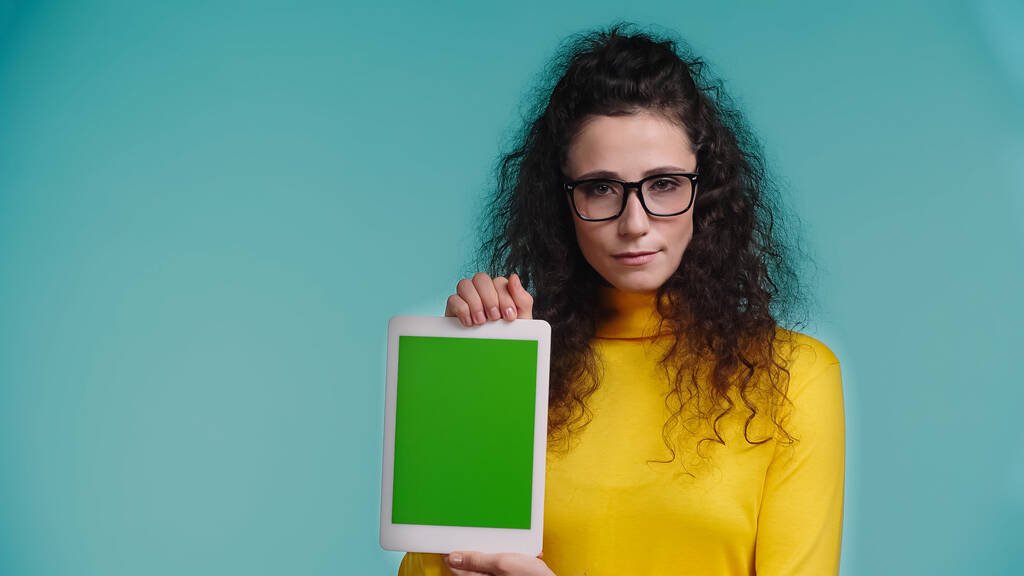 mladá žena v brýlích drží digitální tablet se zelenou obrazovkou izolované na modré  - Fotografie, Obrázek