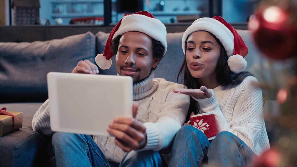 feliz africano americano hombre cerca de mujer enviando aire beso y mirando digital tablet durante video llamada - Foto, Imagen