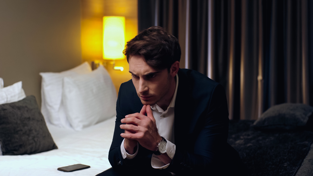 Nachdenklicher Geschäftsmann sitzt auf Bett im Hotelzimmer - Foto, Bild