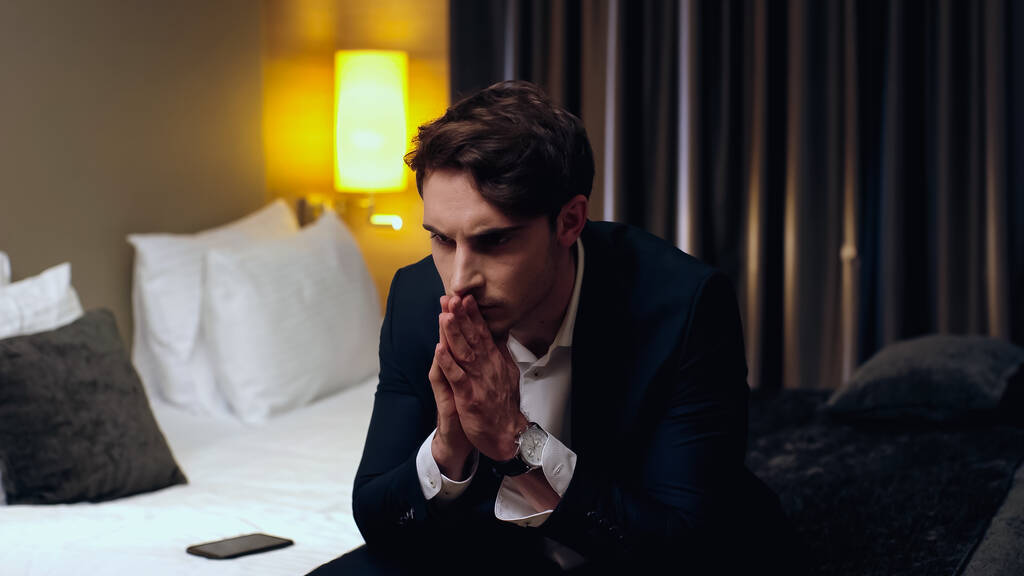 preocupado hombre de negocios sentado con las manos en oración en la habitación de hotel - Foto, Imagen