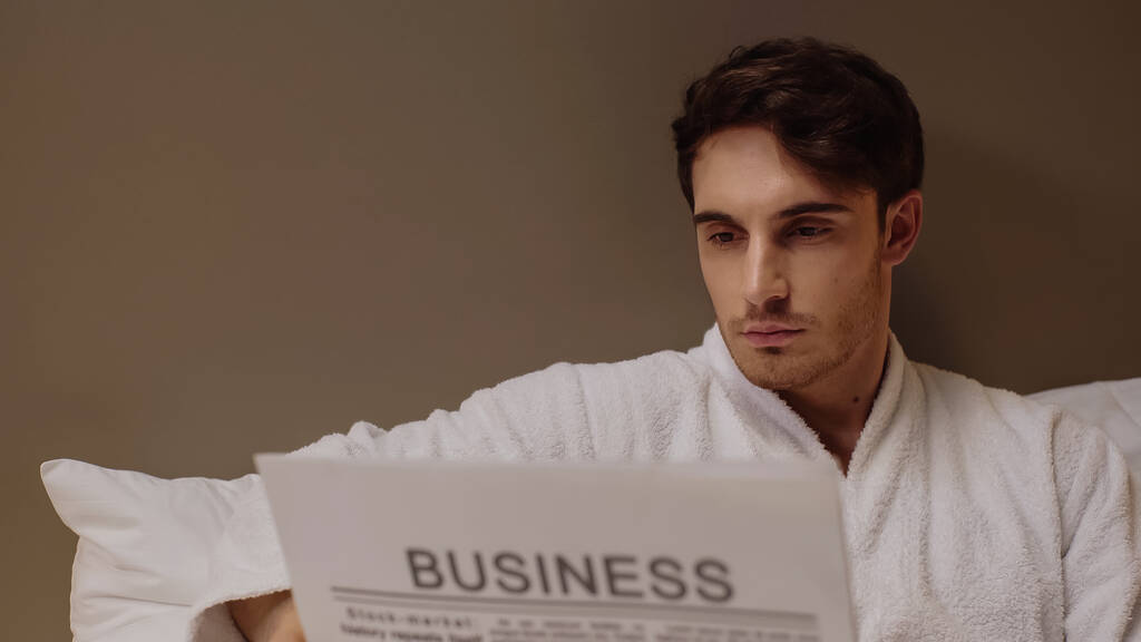 focused man reading business newspaper while resting in hotel room - Photo, Image
