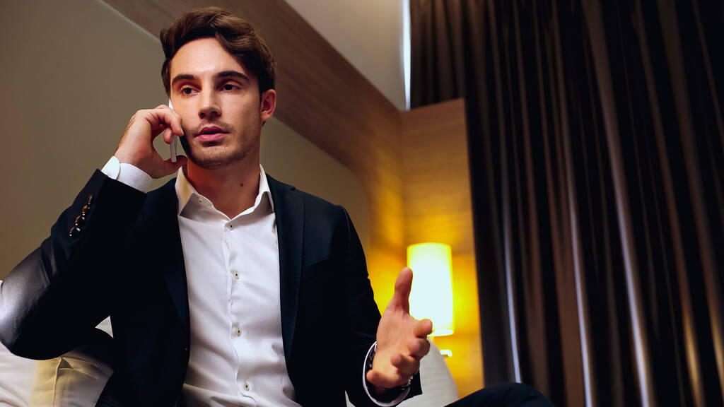 üzletember gesztikulál, miközben beszél mobilon a hotelszobában - Fotó, kép