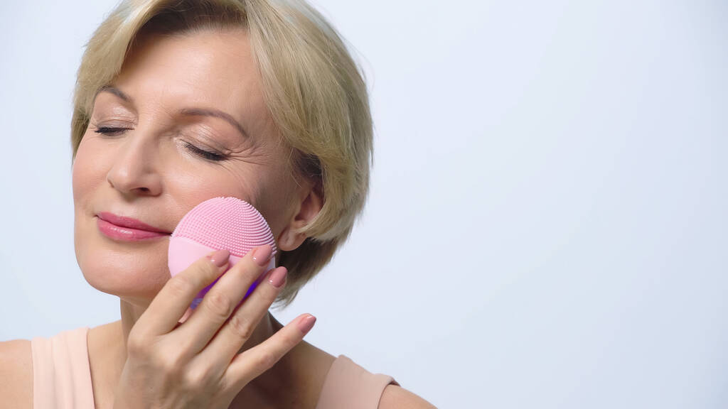 piacere donna di mezza età utilizzando detergente siliconico sul viso isolato su bianco - Foto, immagini