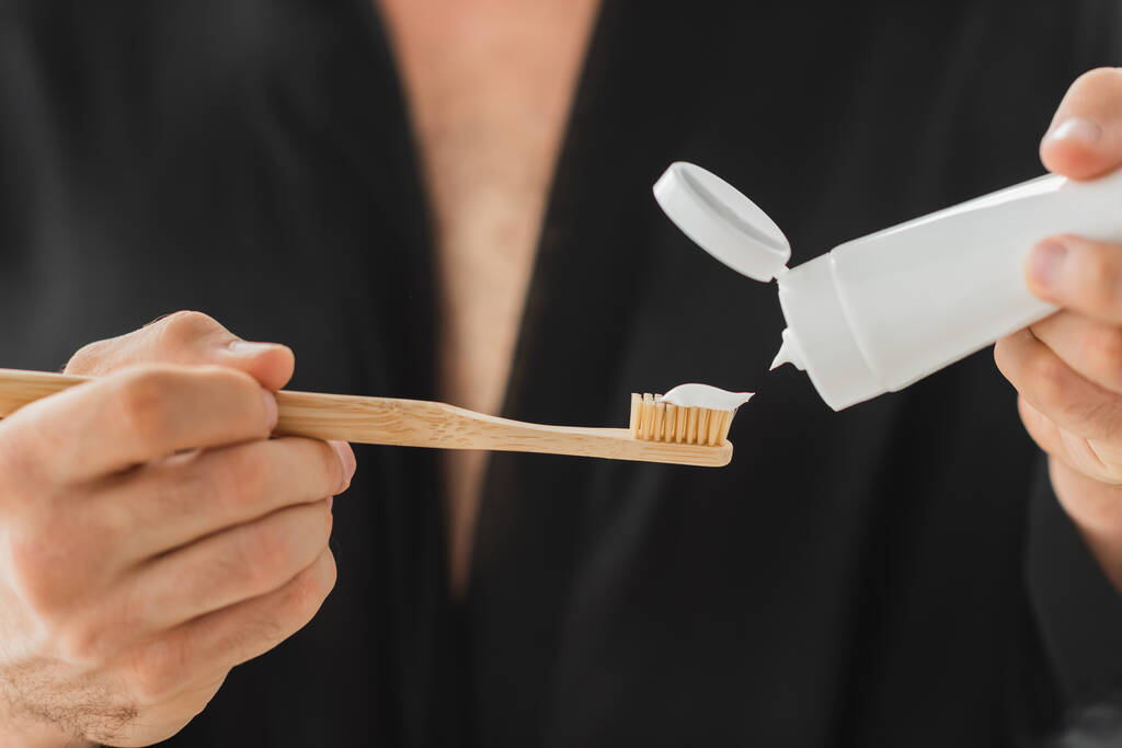 Cropped view of blurred man pouring toothpaste on toothbrush  - Photo, Image
