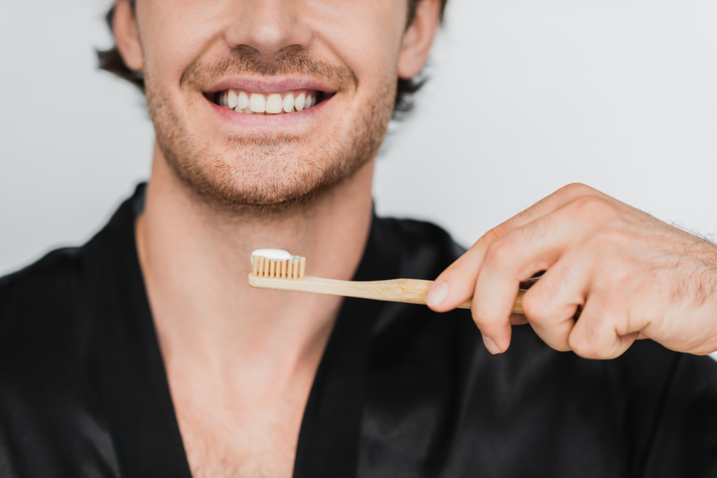 Vista recortada del hombre sonriente en bata sosteniendo cepillo de dientes aislado en gris  - Foto, imagen