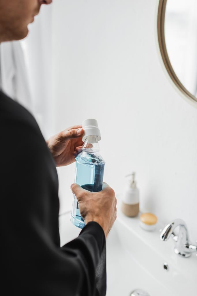 Ausgeschnittene Ansicht eines Mannes mit Flasche Mundwasser im Badezimmer  - Foto, Bild