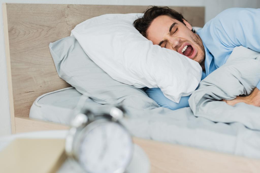 Mann gähnt, während er morgens mit geschlossenen Augen im Bett liegt  - Foto, Bild