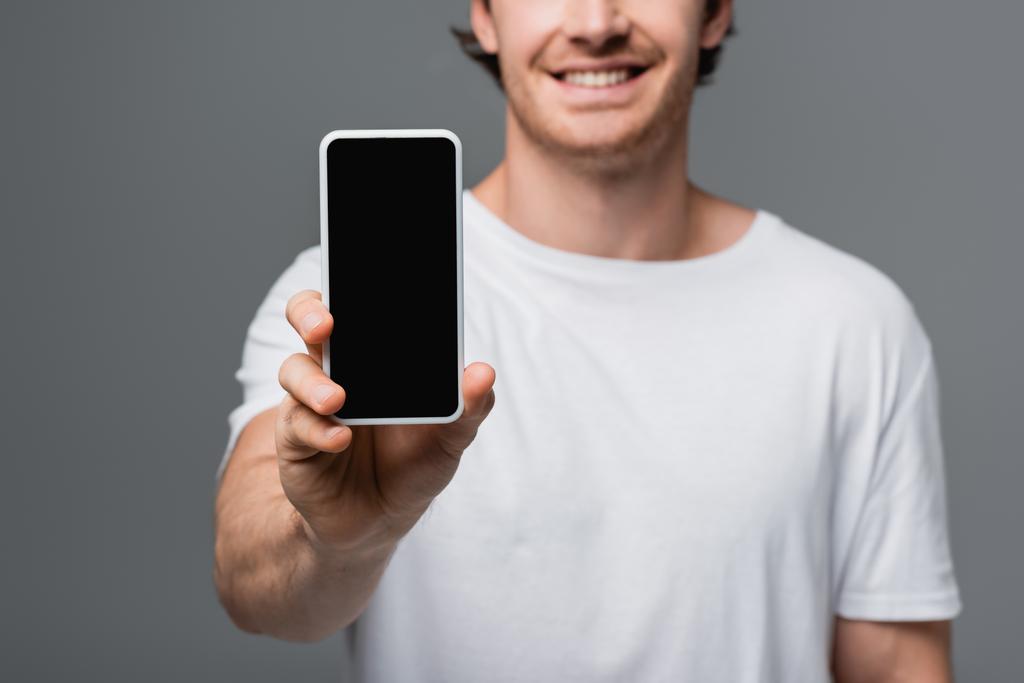 Ausgeschnittene Ansicht des Smartphones in der Hand eines verschwommenen lächelnden Mannes isoliert auf grau  - Foto, Bild