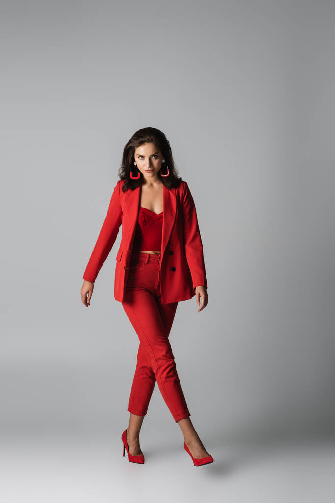 pełna długość młoda stylowa kobieta w czerwonych obcasach i strój chodzenie na szarym - Zdjęcie, obraz