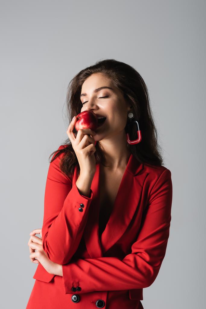 赤いスーツの幸せな女性は灰色で隔離された新鮮なリンゴを食べる  - 写真・画像
