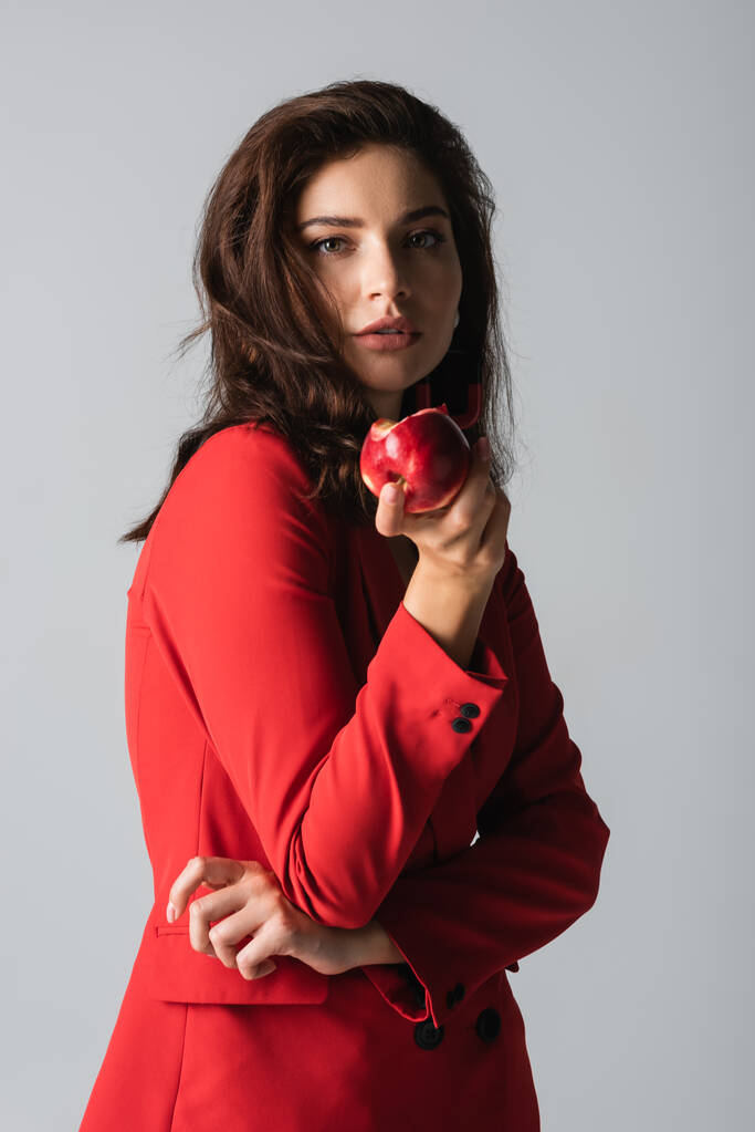 jonge vrouw in trendy pak met rode appel geïsoleerd op grijs  - Foto, afbeelding