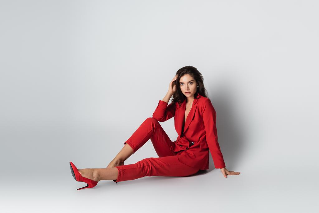 piena lunghezza della donna alla moda in abito rosso in posa mentre seduto sul grigio - Foto, immagini