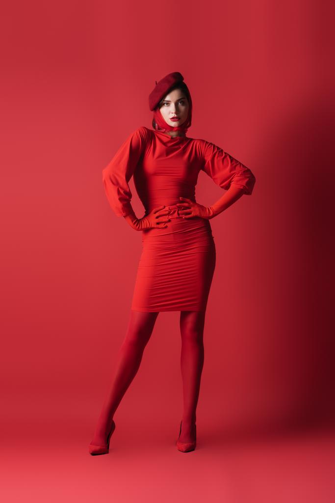 pleine longueur de jeune femme brune en béret posant avec les mains sur les hanches sur le rouge - Photo, image