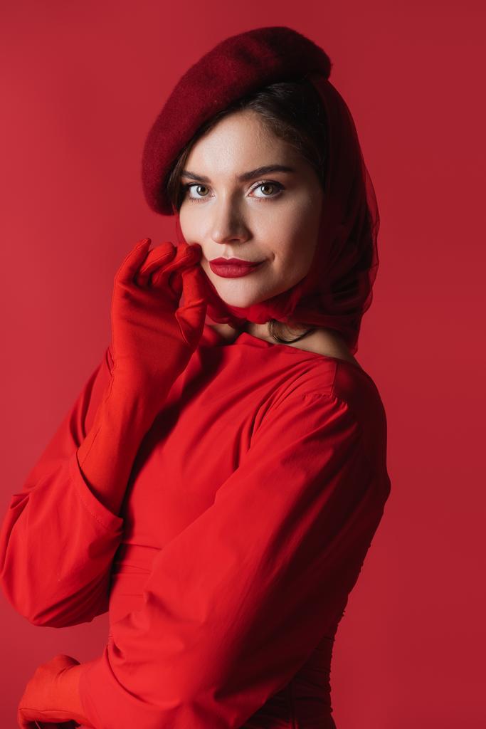 elegant woman in beret and dress looking at camera isolated on red - Photo, Image