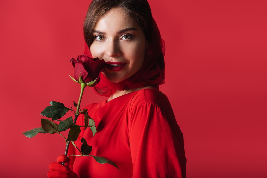 vidám fiatal nő kesztyű és fejkendő tartó rózsa elszigetelt piros - Fotó, kép