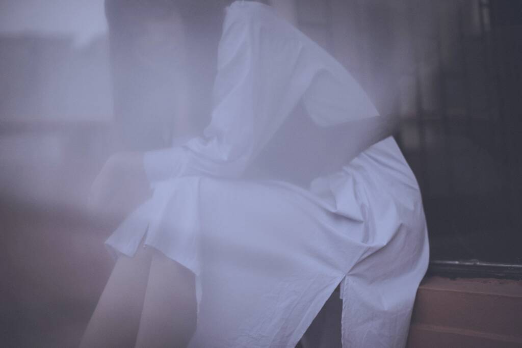 a young man in a white dress and a veil on a bed - 写真・画像
