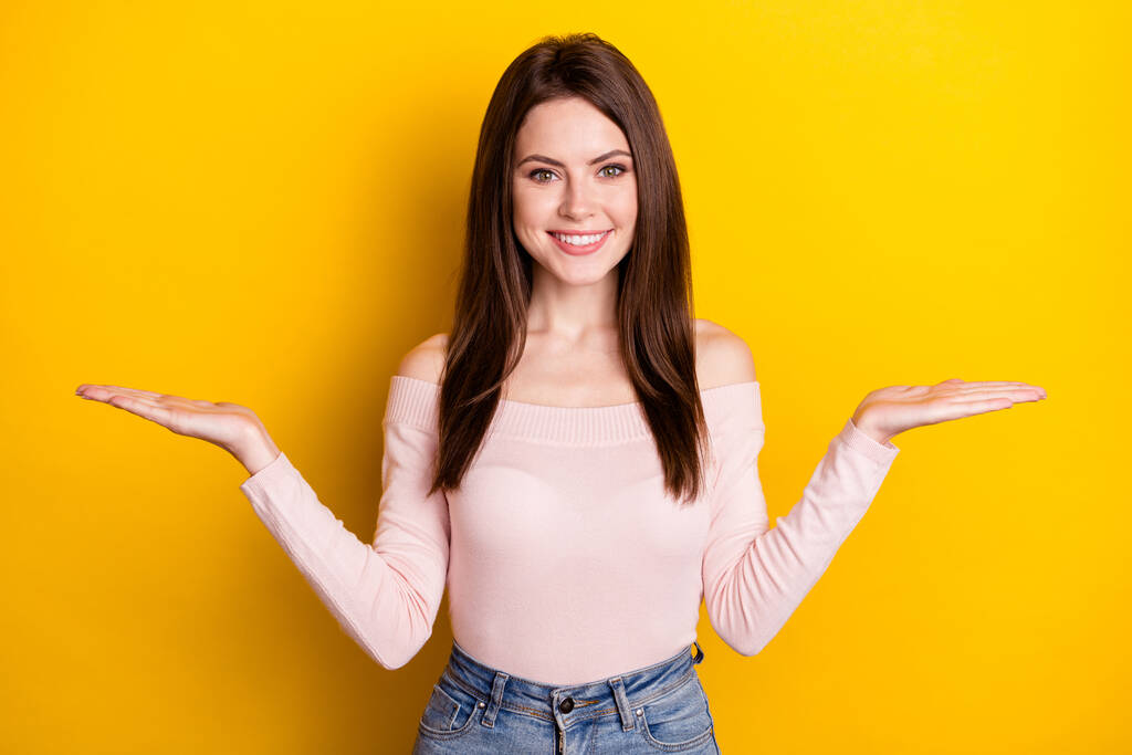 Foto de jovem bela menina sorridente de mãos dadas em equilíbrio publicidade oferta de produto isolado no fundo de cor amarela - Foto, Imagem