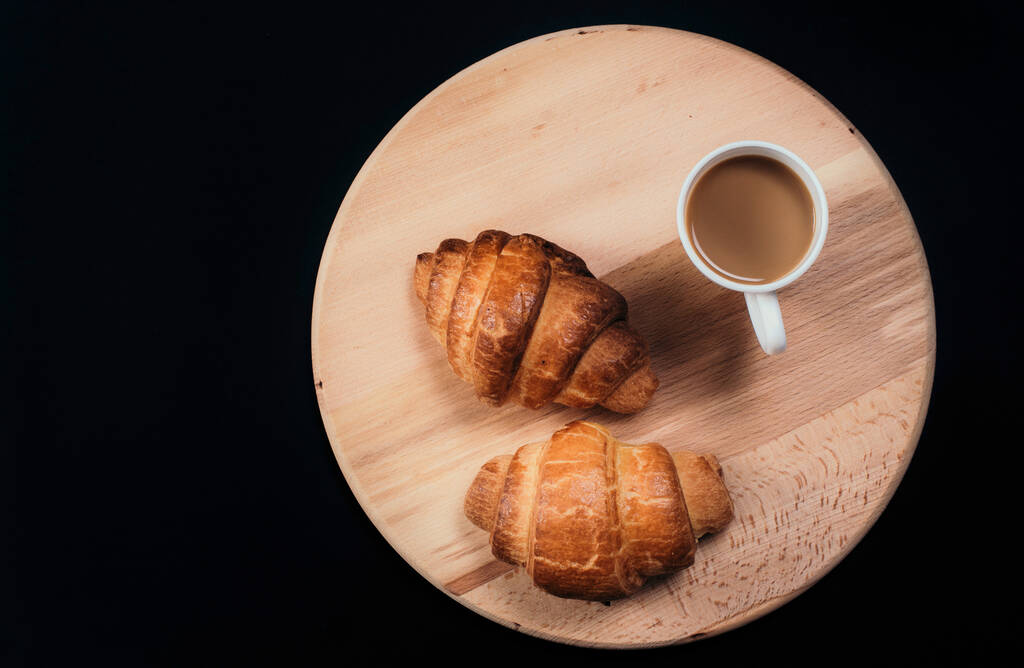 De cima vista de dois croissants frescos e caneca com café colocado em guardanapo no fundo preto da mesa
 - Foto, Imagem