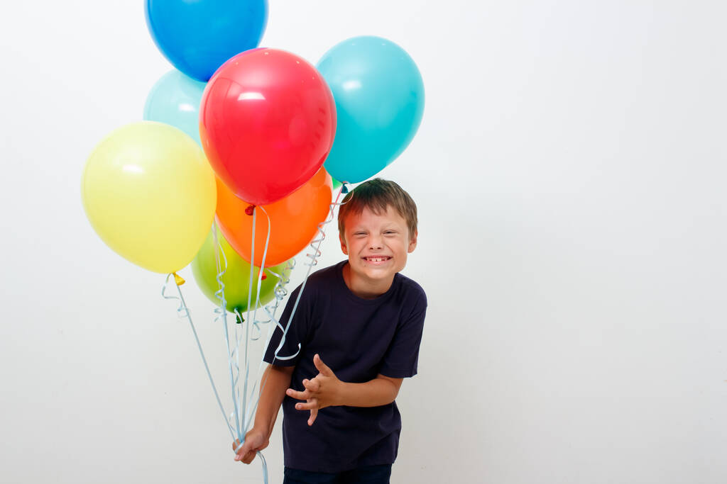 Gelukkige achtjarige jongen met een armvol felgekleurde ballonnen viert zijn verjaardag. lichte achtergrond. Kopieerruimte. - Foto, afbeelding