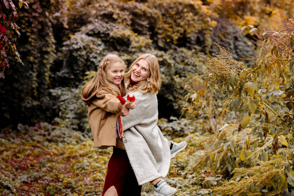 Uma jovem mãe loira adulta com uma filha de 7 anos em um passeio no parque de outono abraçar e rir - Foto, Imagem