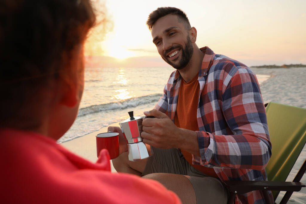 Пара наслаждается горячим напитком на берегу моря. Пляжный кемпинг - Фото, изображение