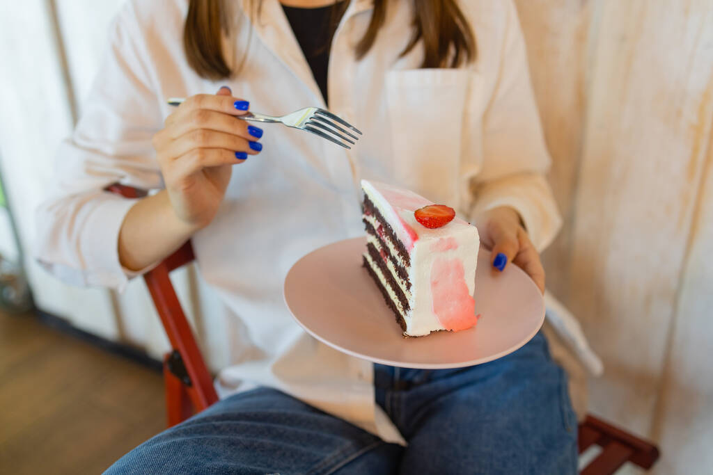 Νεαρή γυναίκα τρώει επιδόρπιο στο εστιατόριο, κοντινό πλάνο. Κάτοψη των θηλυκών χεριών κρατώντας πιρούνι με κομμάτι κερασόπιτας δίπλα στο πιάτο με φέτα κέικ. - Φωτογραφία, εικόνα