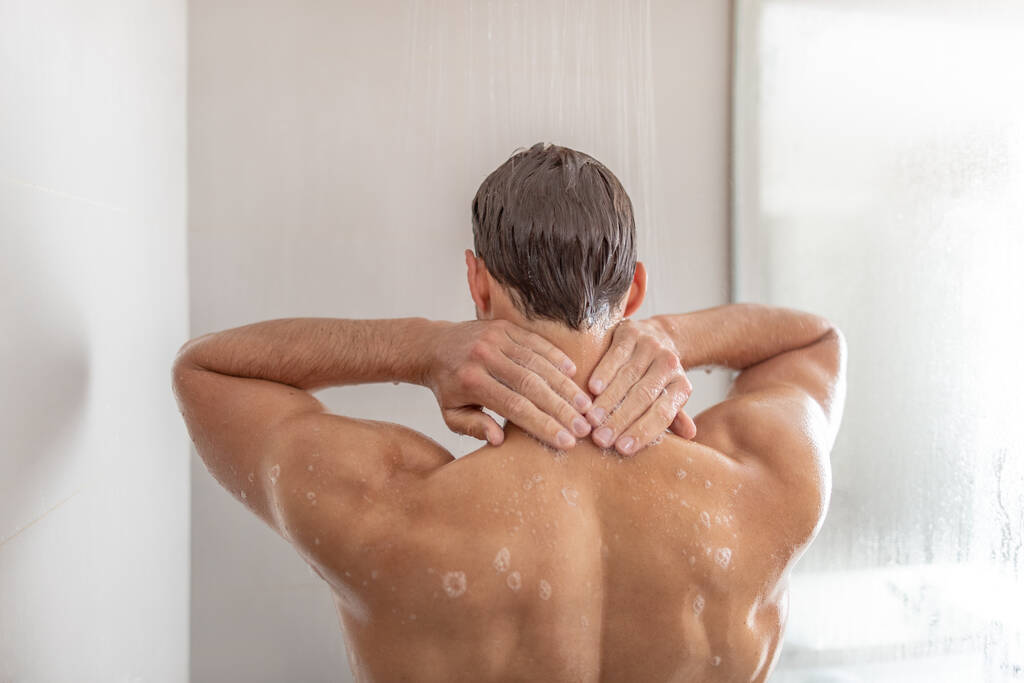 Hombre tomando una ducha lavando el cabello en la bañera de hidromasaje de lujo. Duchándose joven tocando la nuca en casa. Cuidado corporal belleza masculina rutina de la mañana. Condominio o estilo de vida hotelero - Foto, imagen