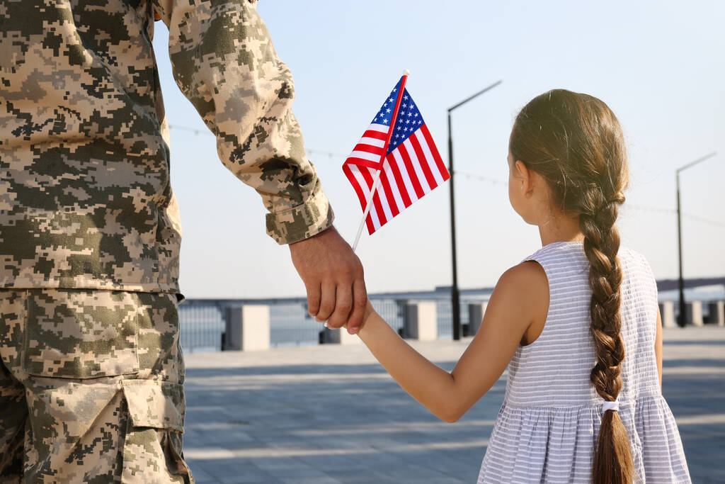 Soldat et sa petite fille avec drapeau américain tenant la main à l'extérieur, vue de dos. Journée des anciens combattants aux États-Unis - Photo, image