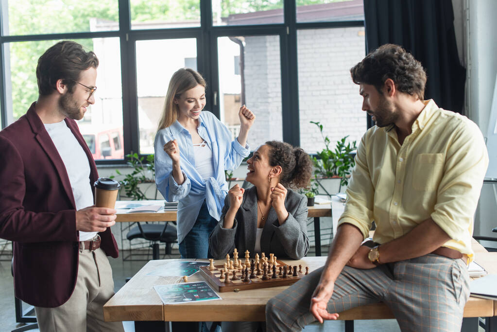 Mezirasové byznysmeny ukazují ano gesto poblíž kolegů hrajících šachy v úřadu  - Fotografie, Obrázek