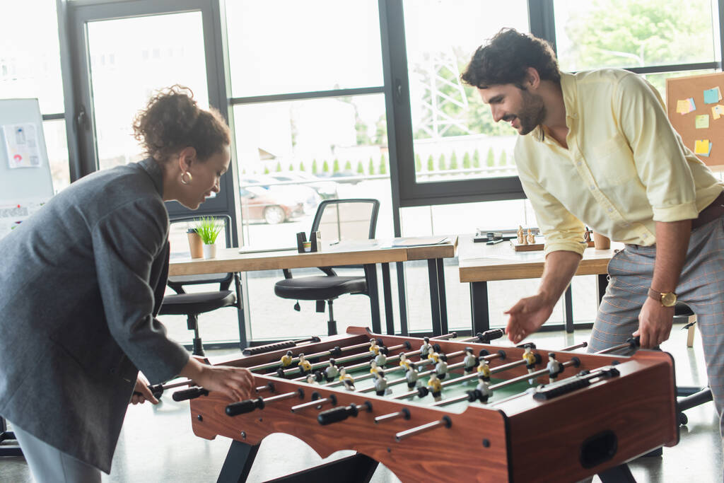 Side view of interracial business people playing table football in office  - Photo, Image