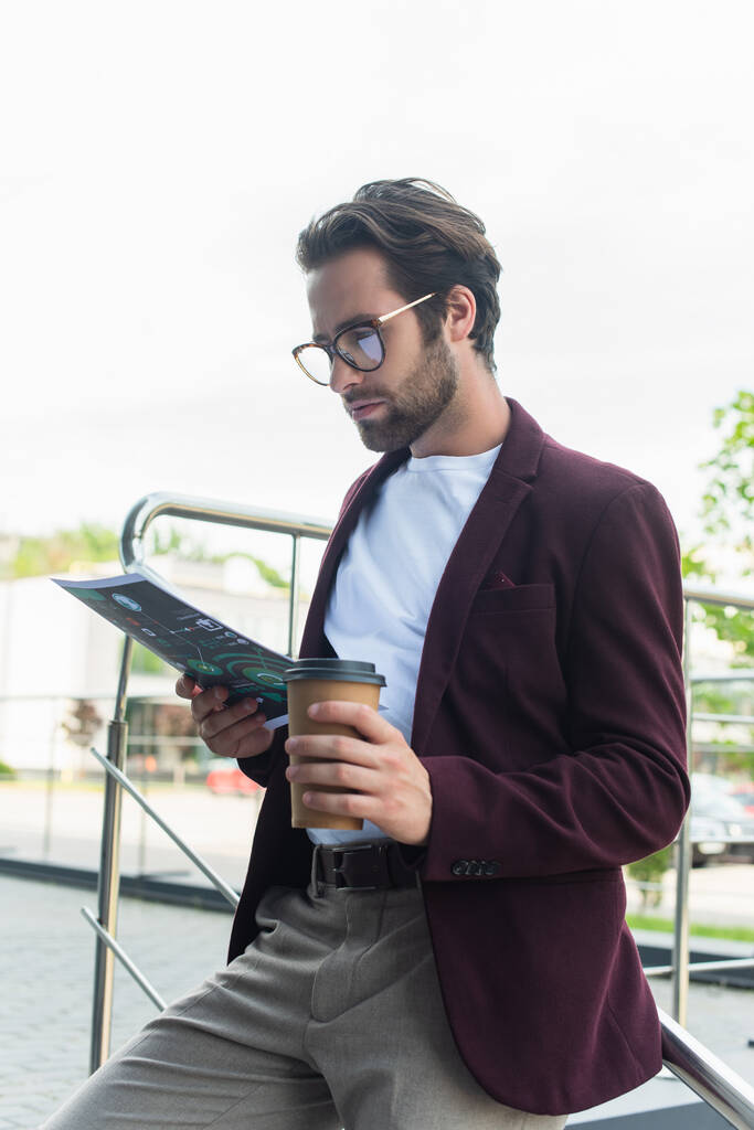 Бізнесмен в формальному одязі та окулярах тримає каву, щоб піти і паперу на відкритому повітрі
  - Фото, зображення