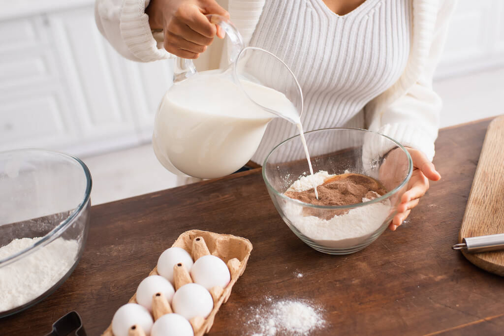 Afro-Amerikalı bir kadının yumurtanın yanına un, mutfakta da kurabiye bıçağının yanına süt dökmesi.  - Fotoğraf, Görsel