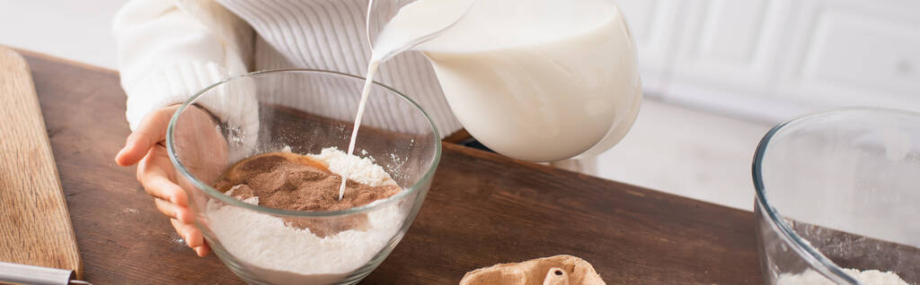 Vista cortada da mulher americana africana derramando leite na farinha com cacau enquanto cozinha na cozinha, banner  - Foto, Imagem