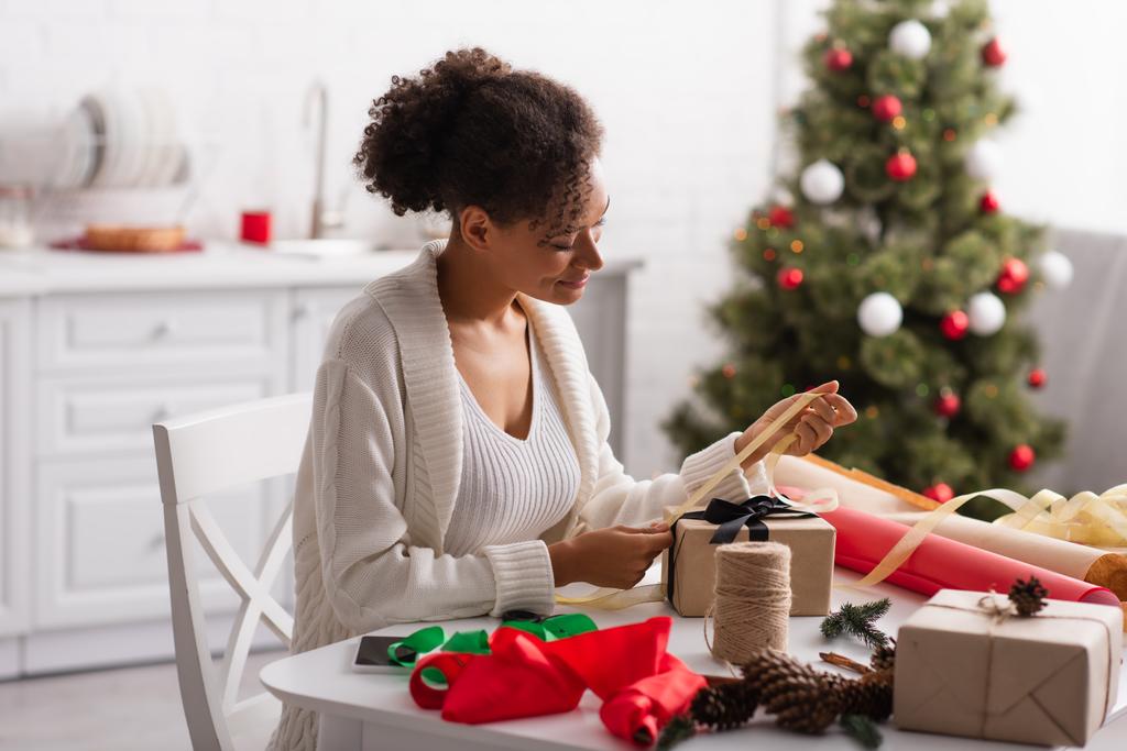 Donna afroamericana decorare regalo di Natale con nastro a casa  - Foto, immagini