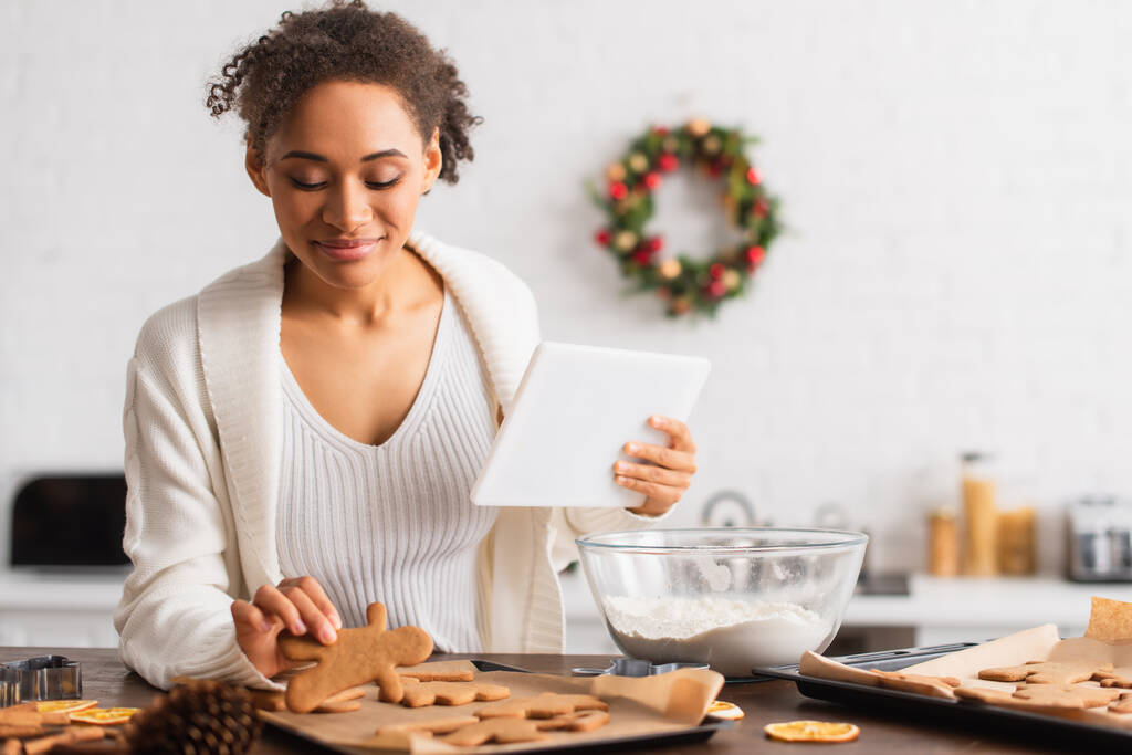 Africano americano segurando tablet digital perto de pão de gengibre e farinha na cozinha  - Foto, Imagem