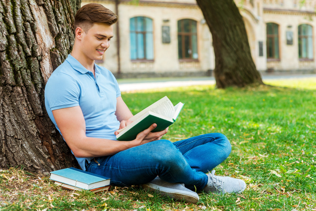 Student reading book and sitting on the grass - Photo, Image