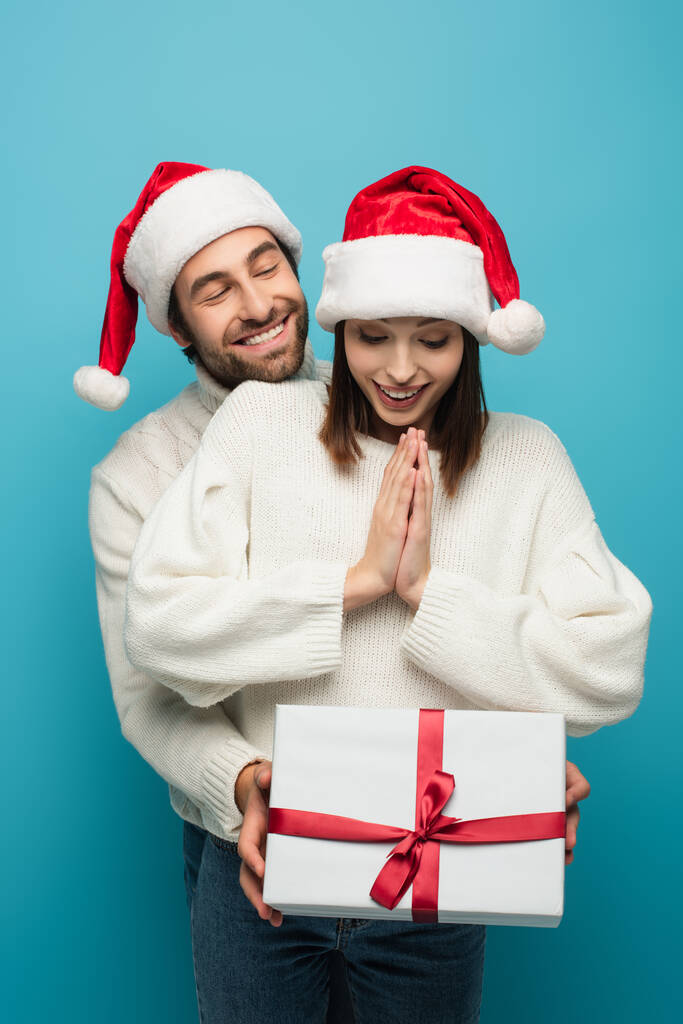 Noel Baba şapkalı gülümseyen adam mavi elbisedeki şaşırmış kadının yanında duruyor. - Fotoğraf, Görsel