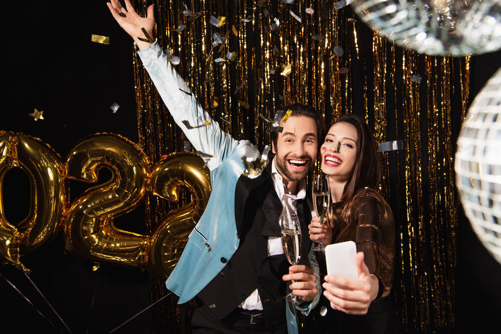 Elegante Frau macht Selfie mit aufgeregtem Mann, während sie Weihnachten auf Schwarz feiert - Foto, Bild