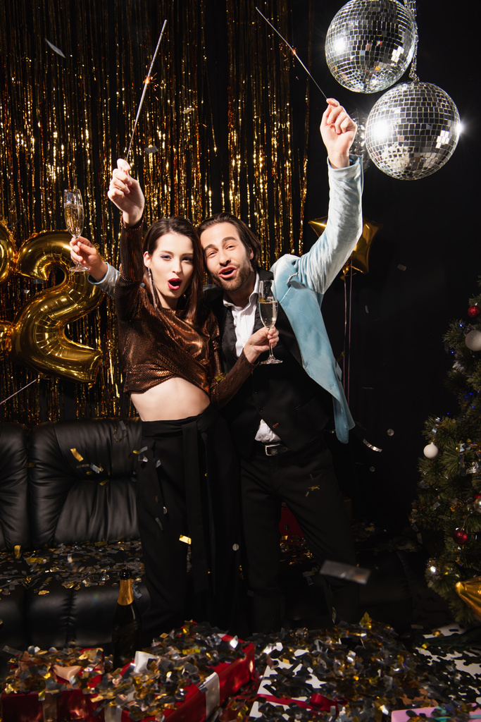 couple excité avec des étincelles et des verres de champagne célébrant Noël sur noir - Photo, image