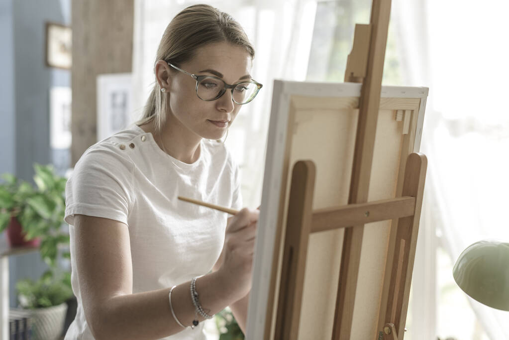 Nuori luottavainen nainen maalaus kankaalle hänen studio, luovuutta ja harrastus käsite - Valokuva, kuva