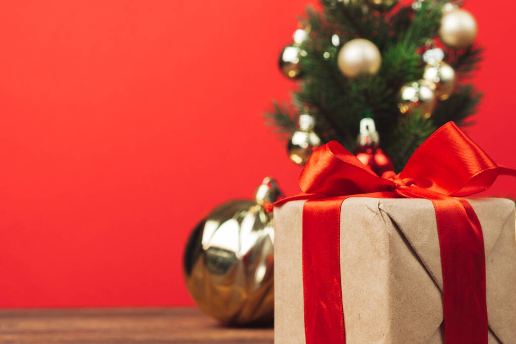Świąteczny prezent owinięty w papier rzemieślniczy z czerwoną wstążką na czerwonym świątecznym tle - Zdjęcie, obraz