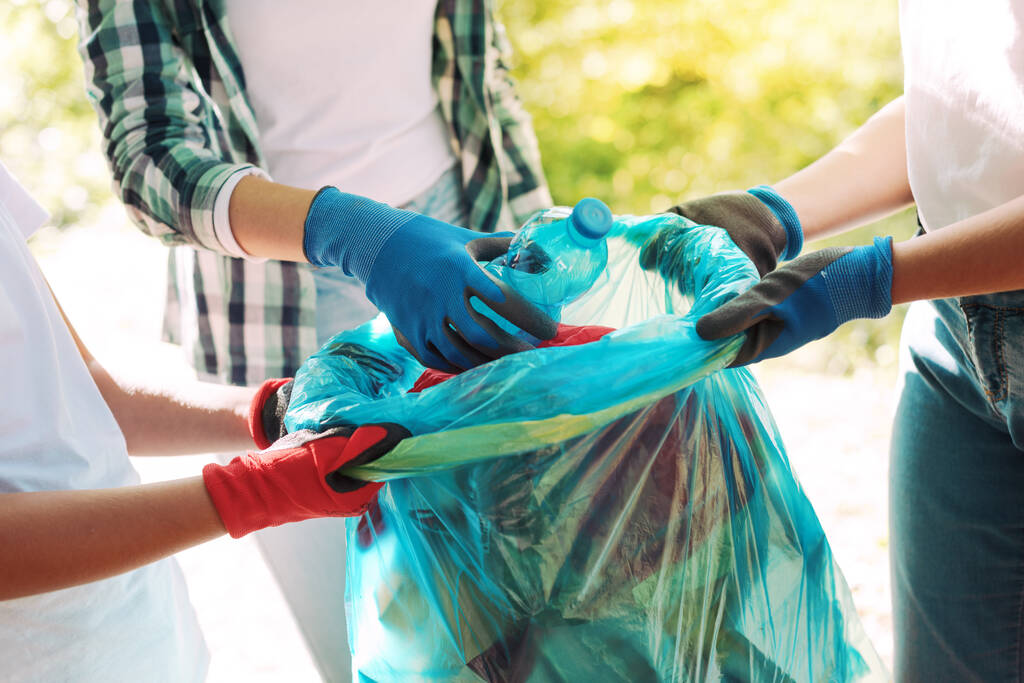 Mladí dobrovolníci uklízejí městský park, dávají odpad do pytle na odpadky. - Fotografie, Obrázek
