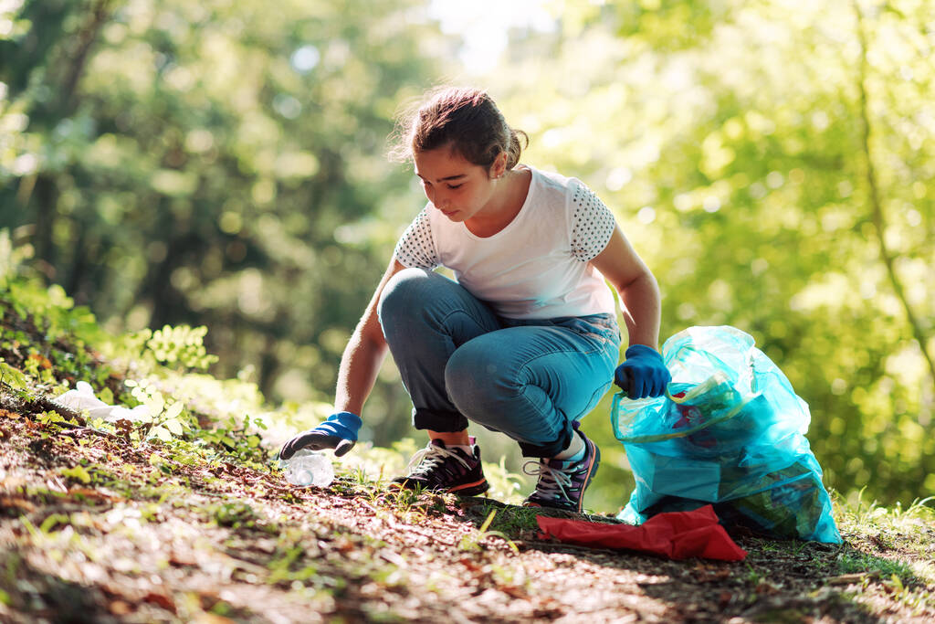 Chica joven limpiando el bosque, ella está recogiendo basura y sosteniendo una bolsa de basura, concepto de protección del medio ambiente - Foto, Imagen