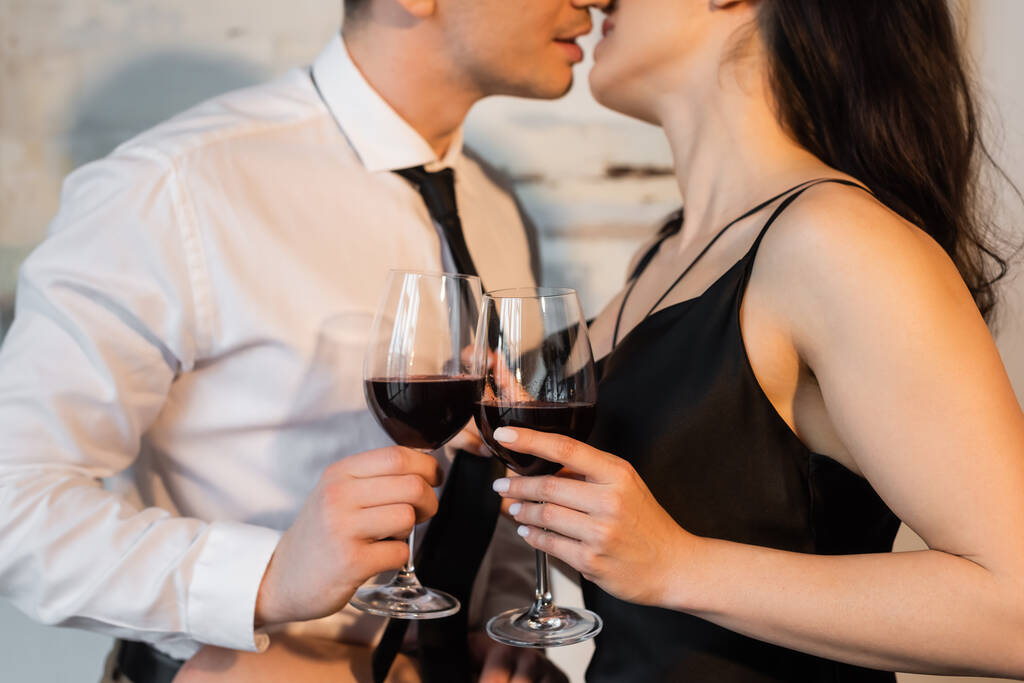 περικοπή άποψη του ζευγαριού κρατώντας ποτήρια του κόκκινου, ενώ φιλιά στο σπίτι - Φωτογραφία, εικόνα