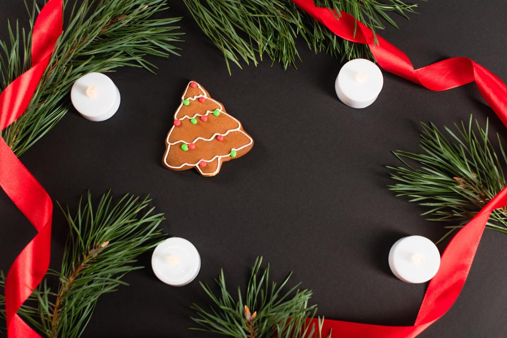 vue du dessus du biscuit au pain d'épice près des bougies, des branches de sapin et du ruban rouge sur le noir  - Photo, image