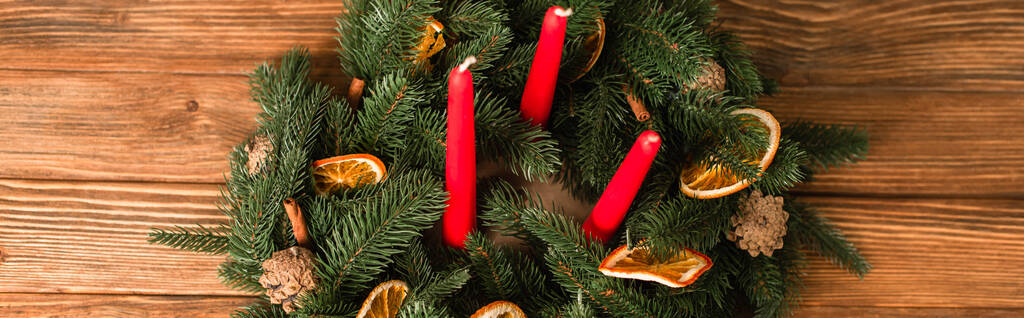 πάνω όψη του στεφανιού των Χριστουγέννων με κόκκινα κεριά και πράσινα κλαδιά σε ξύλινη επιφάνεια, λάβαρο - Φωτογραφία, εικόνα