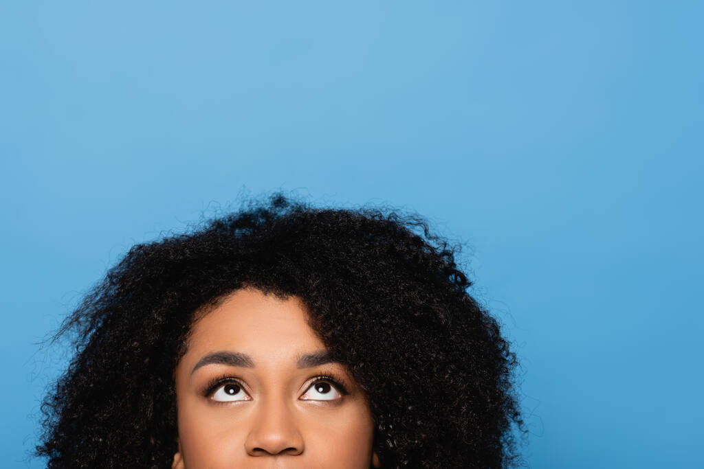 обрізаний вид на кучеряву афроамериканську жінку, яка дивиться вгору ізольовано на синьому
 - Фото, зображення